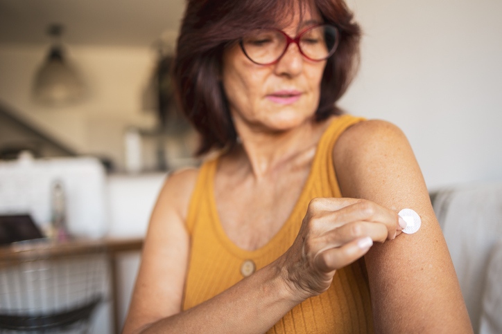 Person applying a small medical adhesive bandage or patch to the upper arm while seated indoors in Sandusky, OH